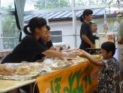 保育園児に二人の生徒が机越しに物を手渡している写真