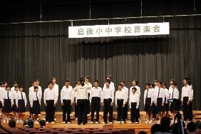舞台で全校生徒で指揮者に合わせて合唱している写真