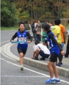 駅伝大会で女子生徒が次の走者にたすきを渡している写真