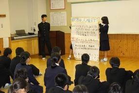 教室で生徒が前に立ち、模造紙を見ながら発表している写真