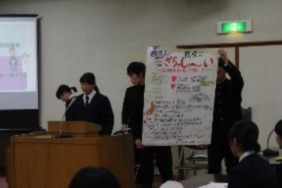 生徒が壇上でモニターと模造紙を使い発表している写真