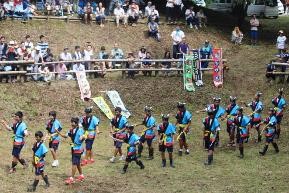 観客が見守る中で、男子生徒が衣装を着て踊りを披露している写真