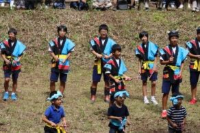 衣装を着た男子生徒が保育所園児と牛突き音頭を踊っている写真