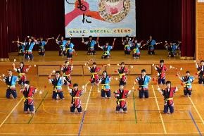体育館の舞台で生徒たちが隊列を作り、踊りを披露している写真