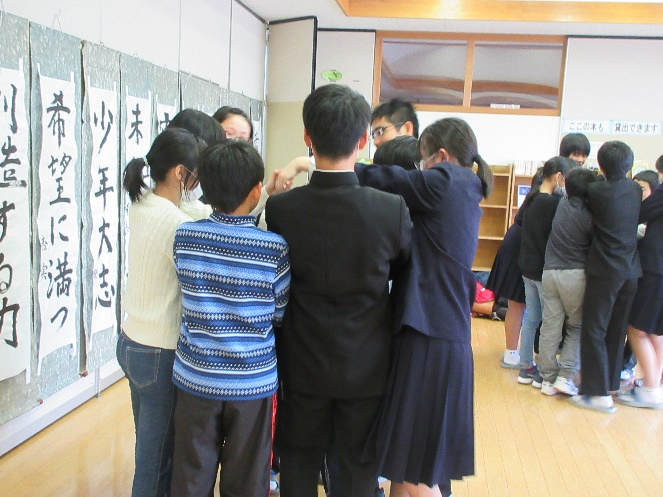 教室で生徒たちが新入生と輪になって手をクロスに繋ぎ遊びを楽しんでいる写真