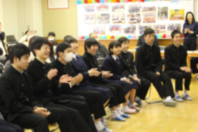 教室で中学校三年の学生たちが下級生が行った催し物を見て拍手をしたり笑って楽しんでいる写真