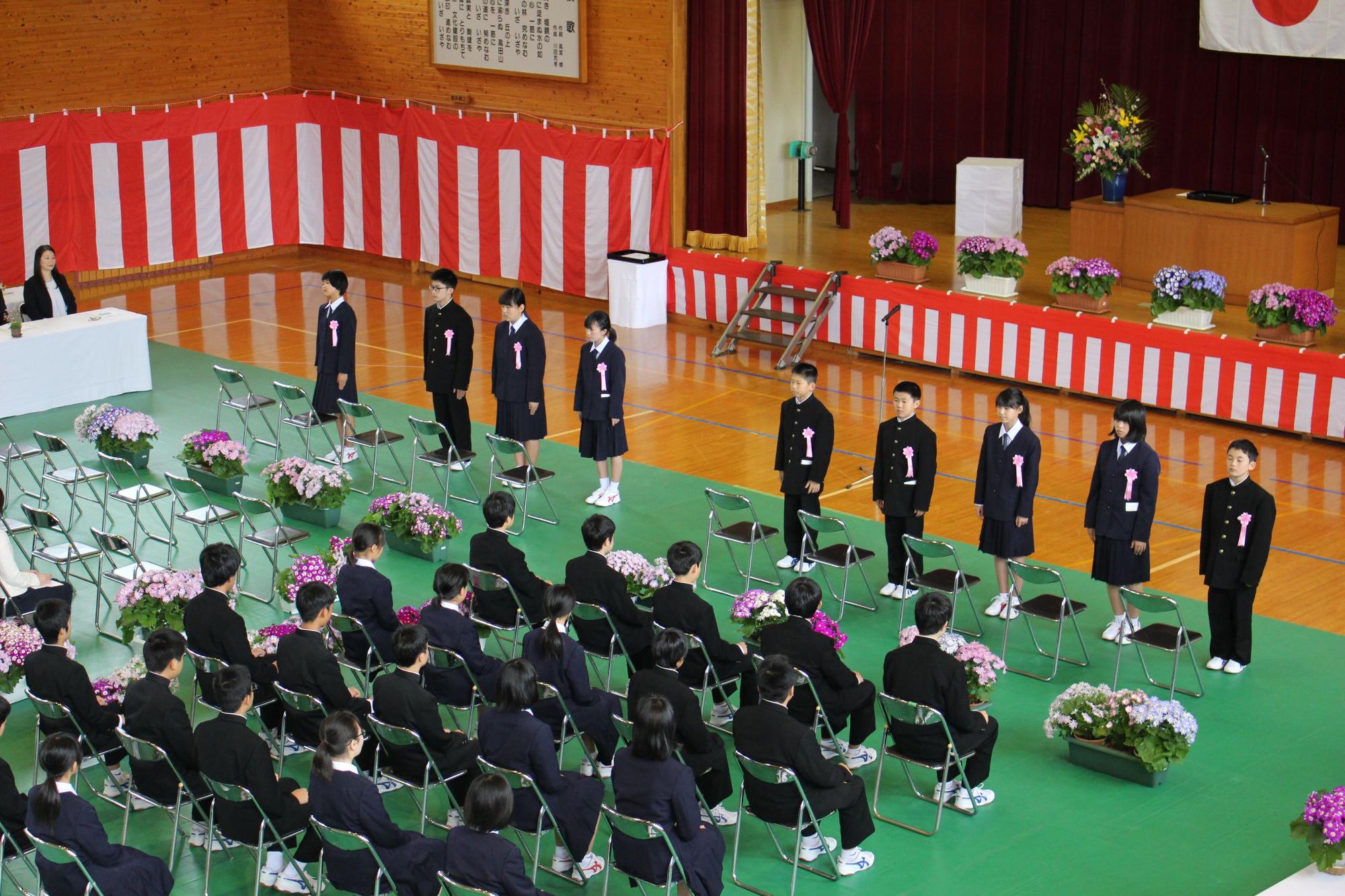 体育館で新入生と在校生が入学式に参加している写真