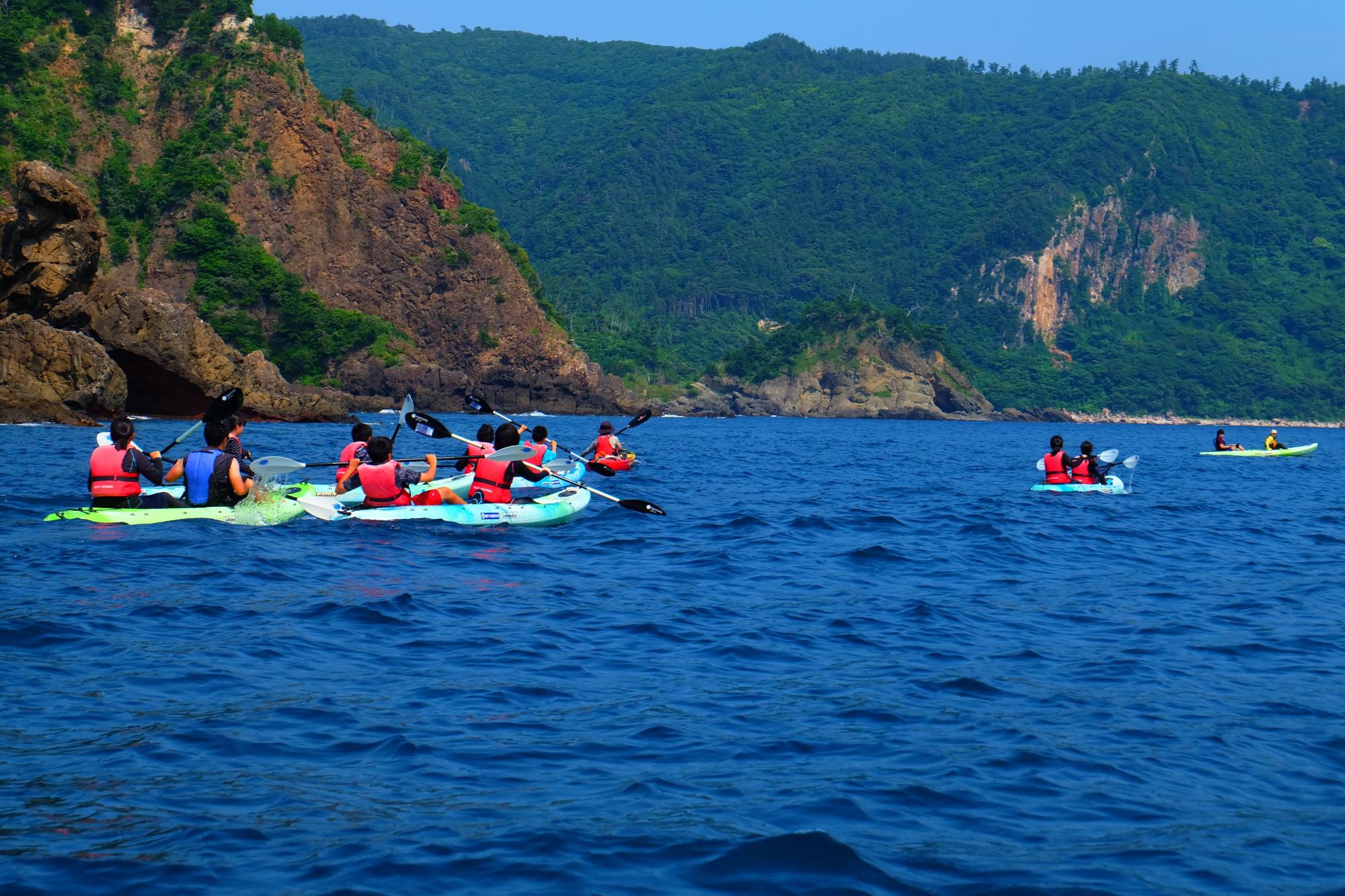 救命胴衣を着けた生徒たちが海上でシーカヤックをしている写真