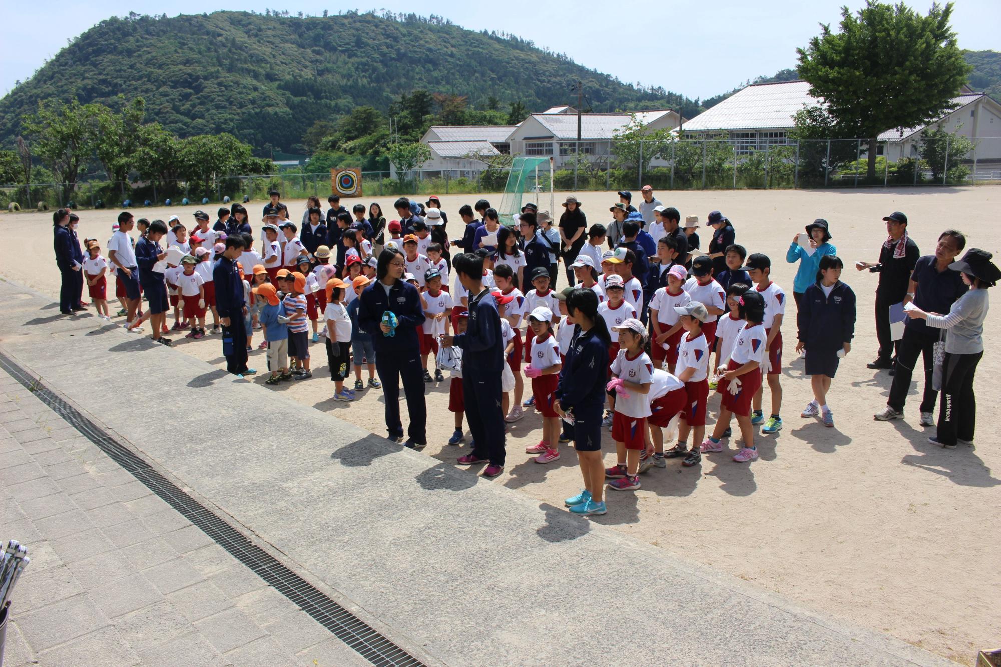 地域の人たちや児童、生徒が一緒にグラウンドに並んでいる写真