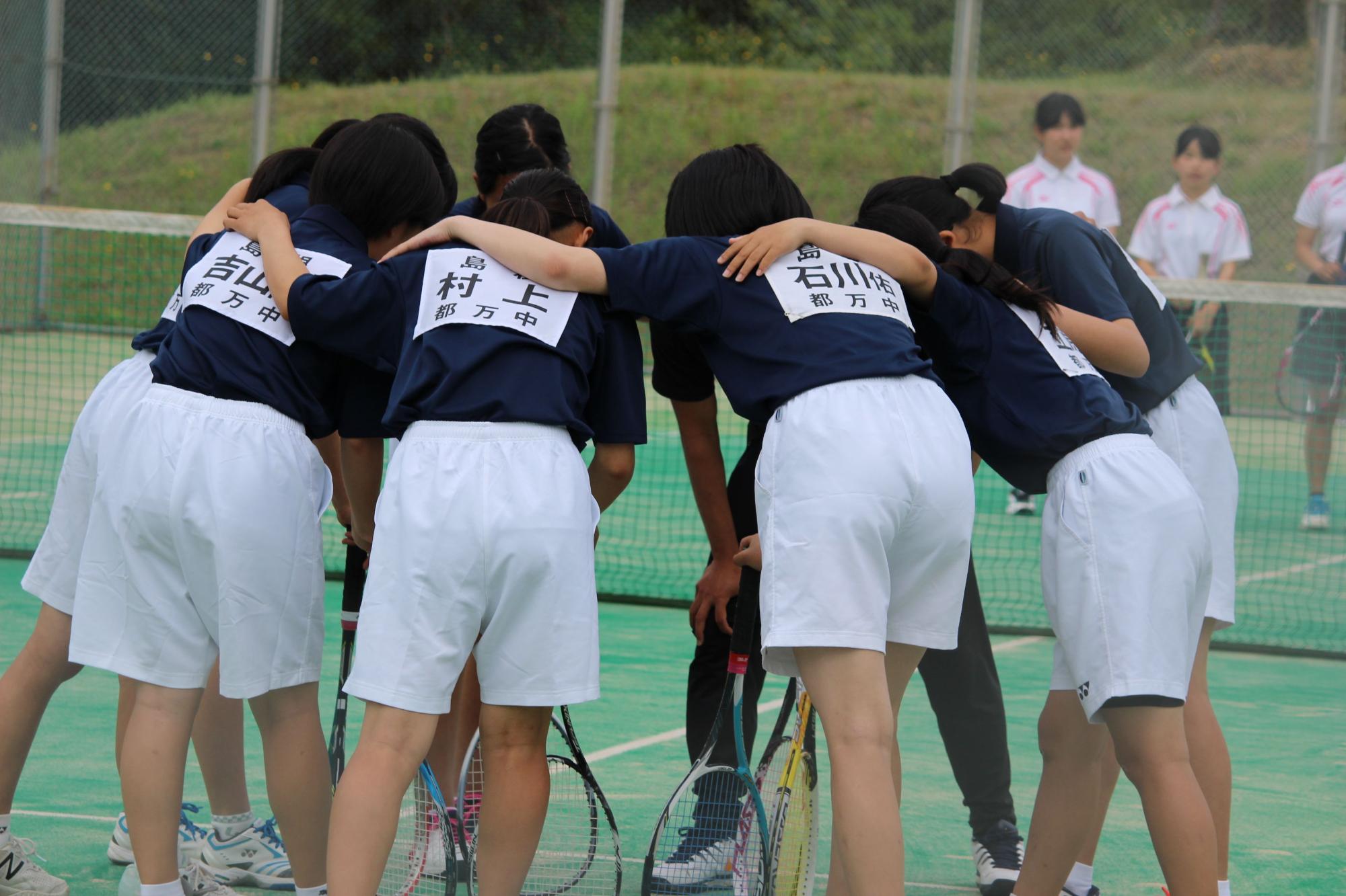 女子テニス部員がコートで円陣を組んでいる写真