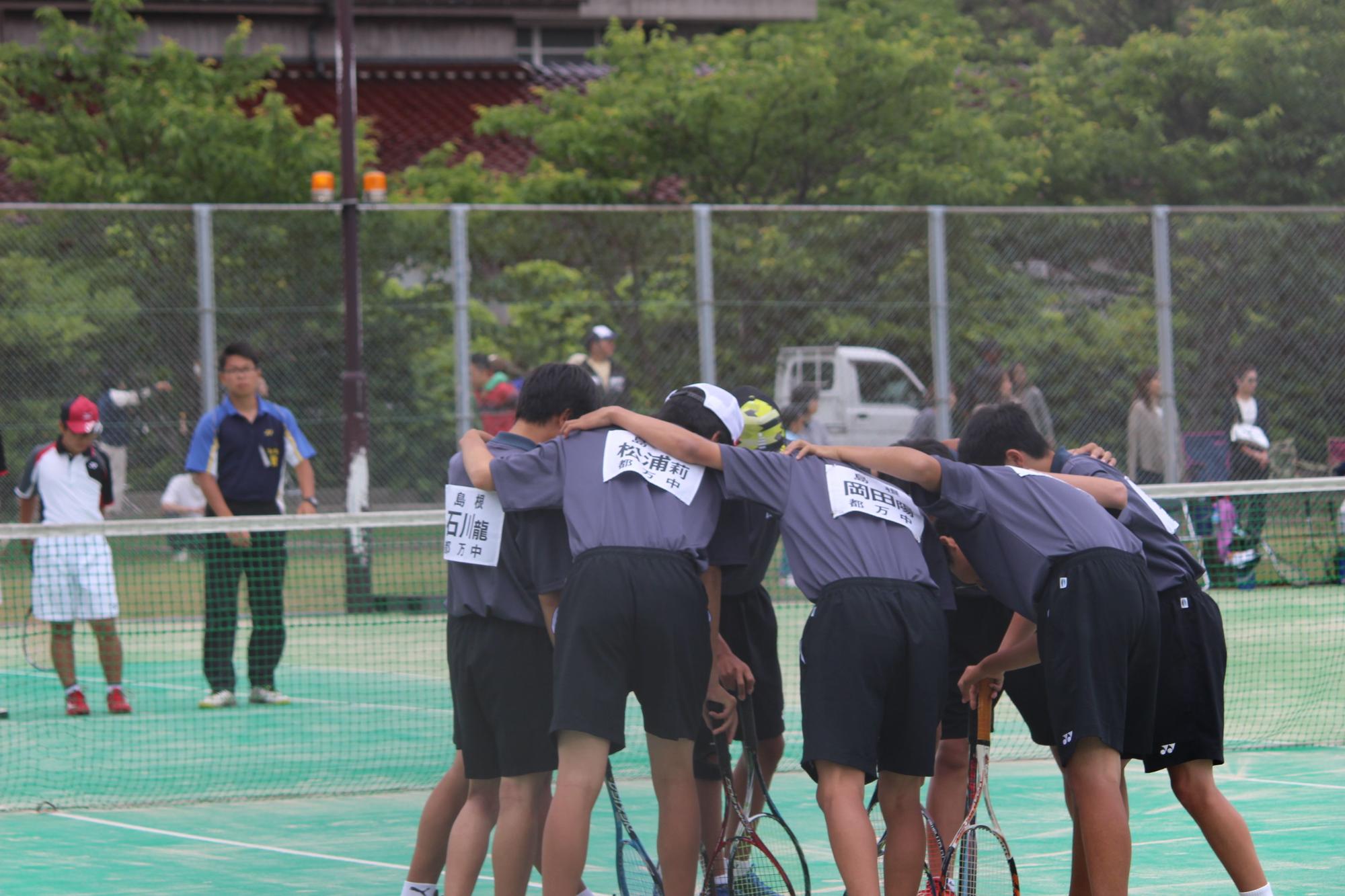 男子テニス部員がコートで円陣を組んでいる写真
