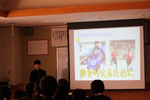 学校の教室で生徒がスクリーンの前に立ち、発表を行っている写真