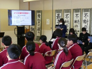 教室で複数の運動着姿の生徒が椅子に座り、スクリーンの映像を見ている写真