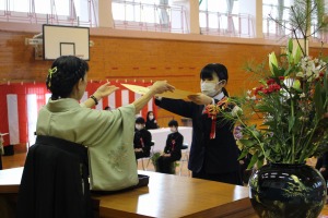 体育館で袴姿の女性がステージ上で卒業証書を生徒に手渡している写真