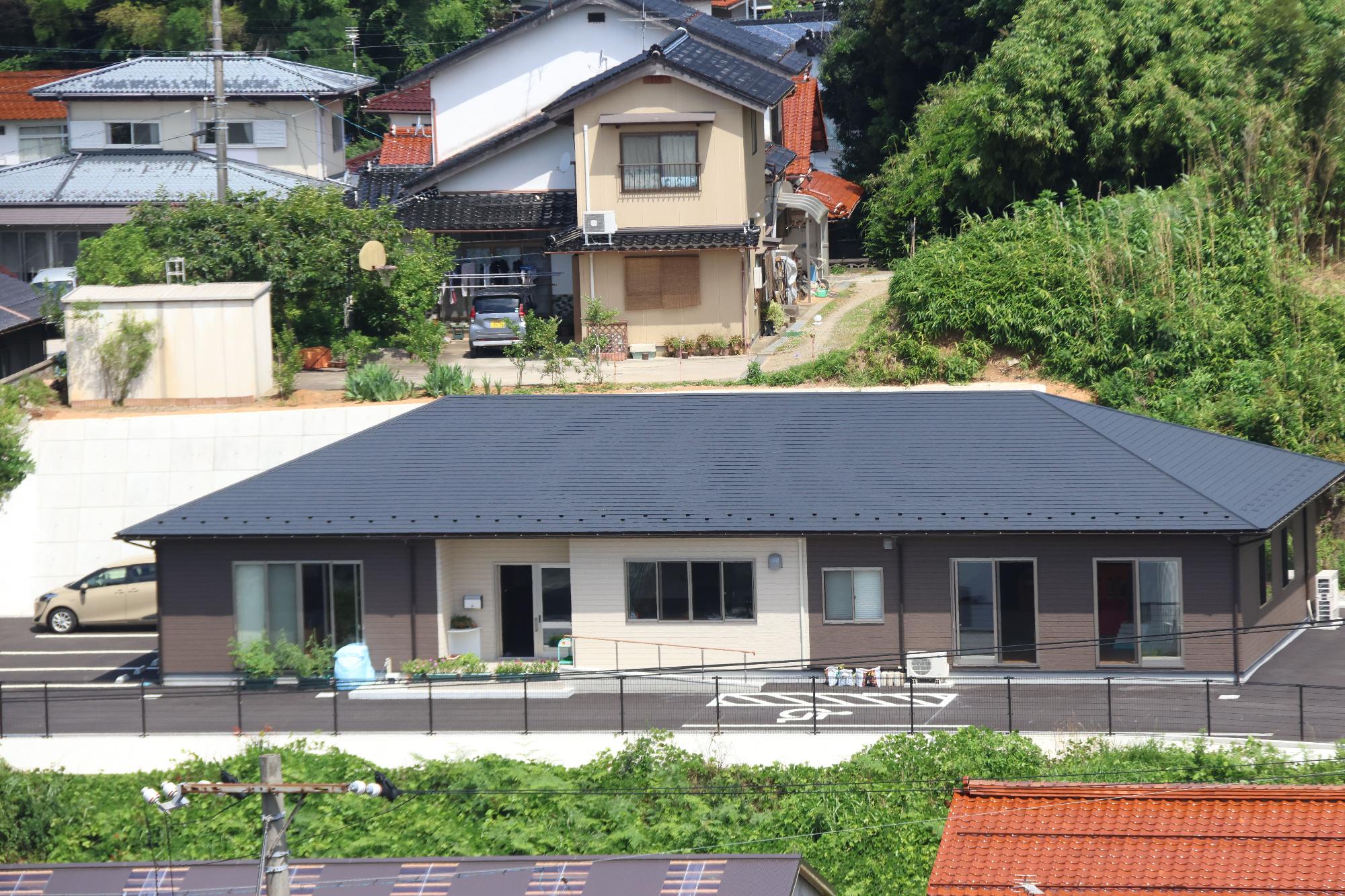 手前に黒い屋根と茶色の壁の横長の建物があり、奥に二件の建物がある写真