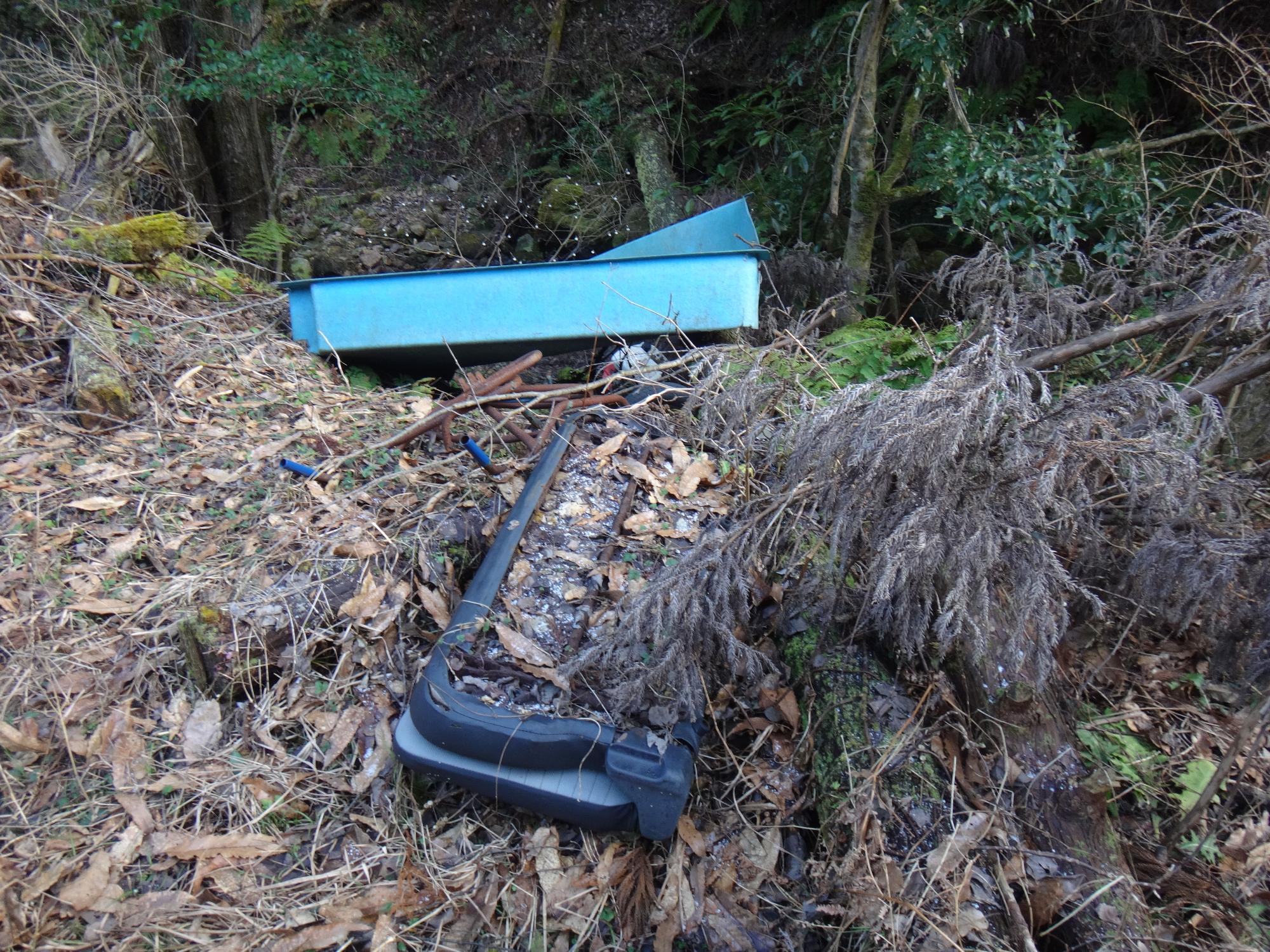 積み重なった枯れ木の中に不法投棄された粗大ゴミの写真