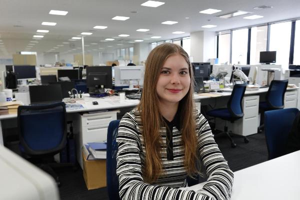 オフィスで、カメラのほうを向き微笑んでいる女性（国際交流員）の写真