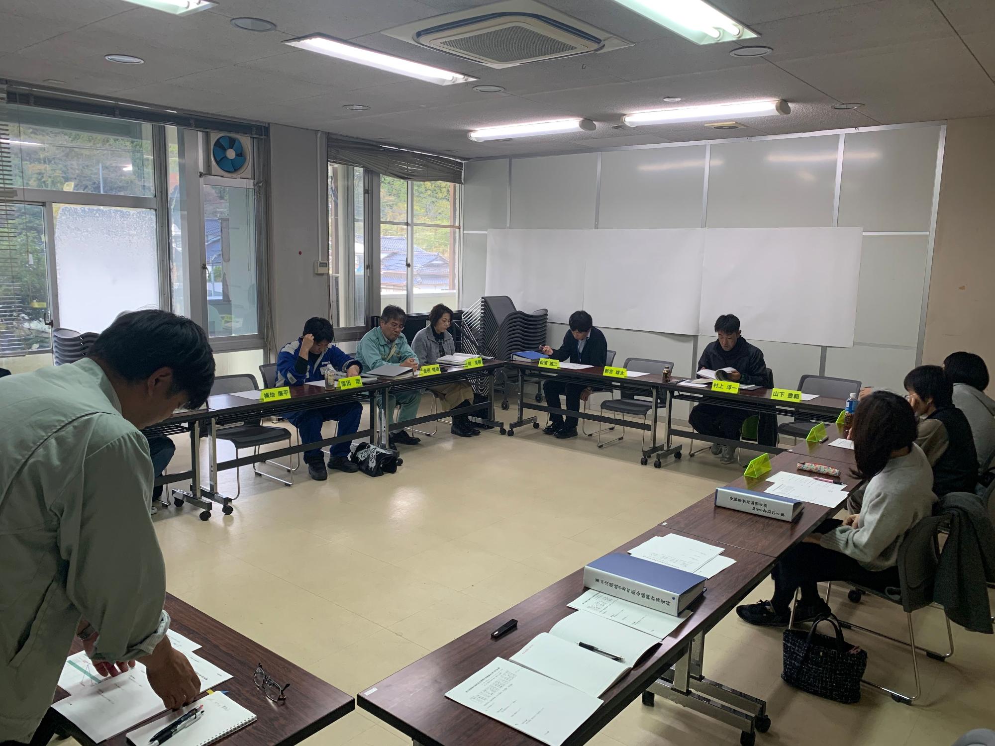 立っている男性が資料を見ながら発言している写真