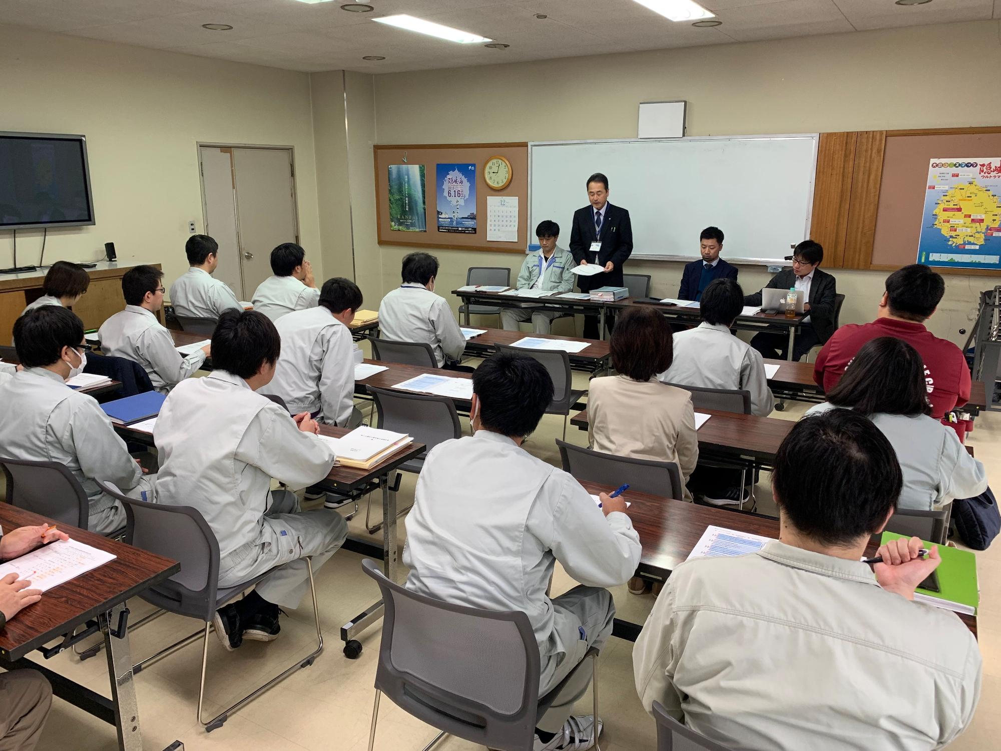 立ち上がって発言しているスーツの男性とそれを聞いている職員たちの写真