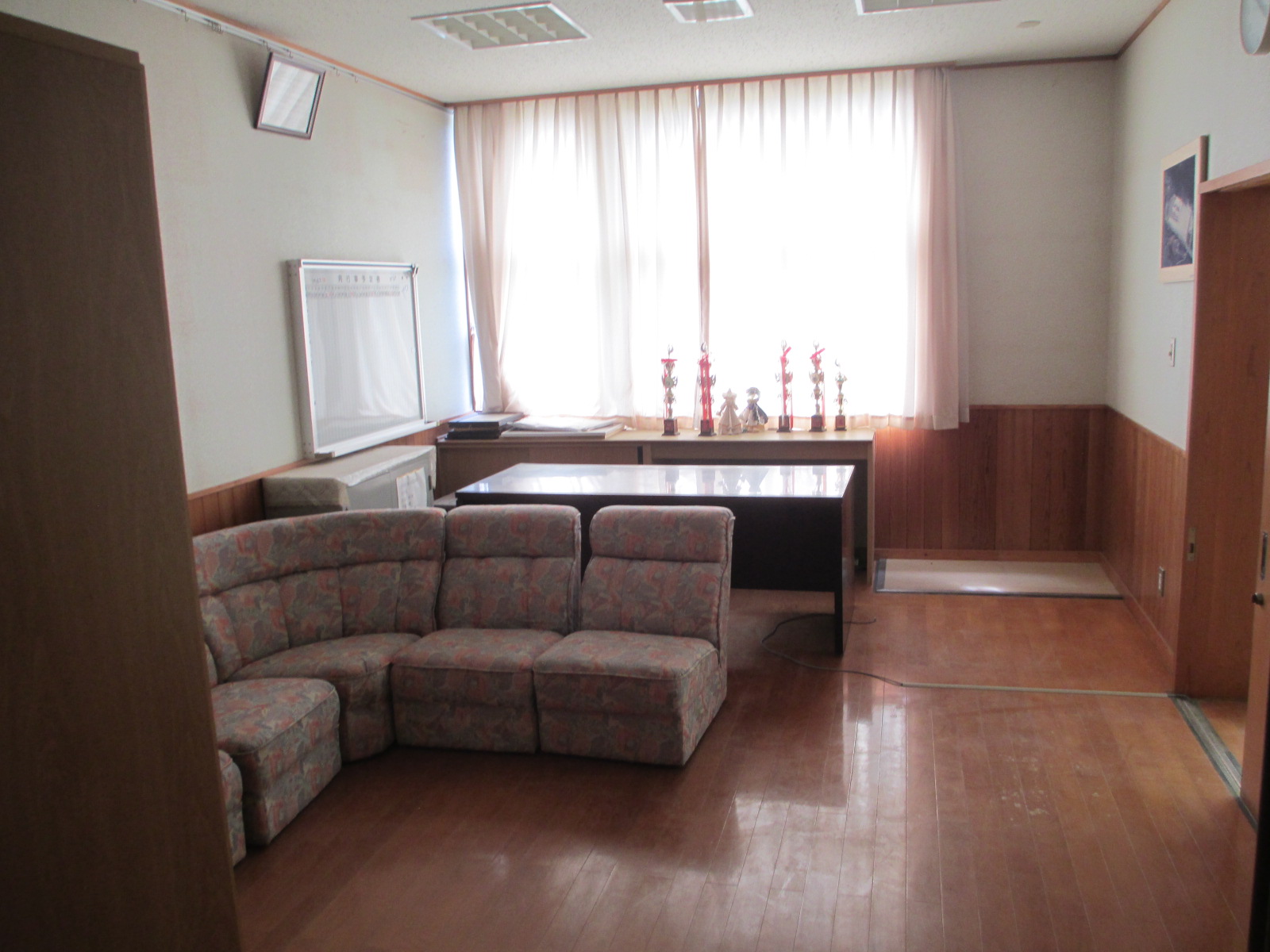 校長室の写真。席の前にはソファーがあり、後にはトロフィーが並んでいる。