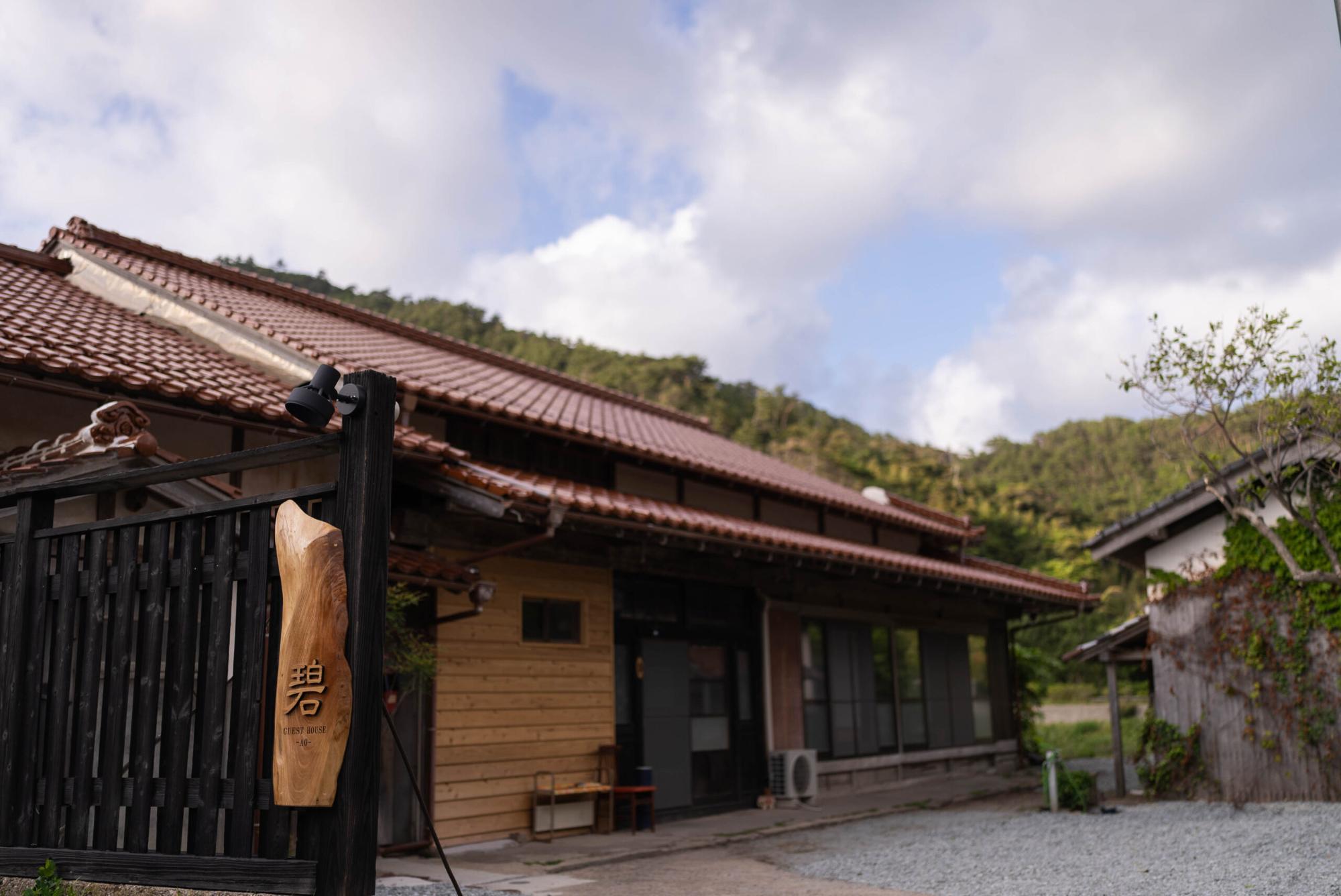 大きな碧の文字がみえる木製の表札が特徴的な、赤い瓦屋根のゲストハウス碧の外観の写真