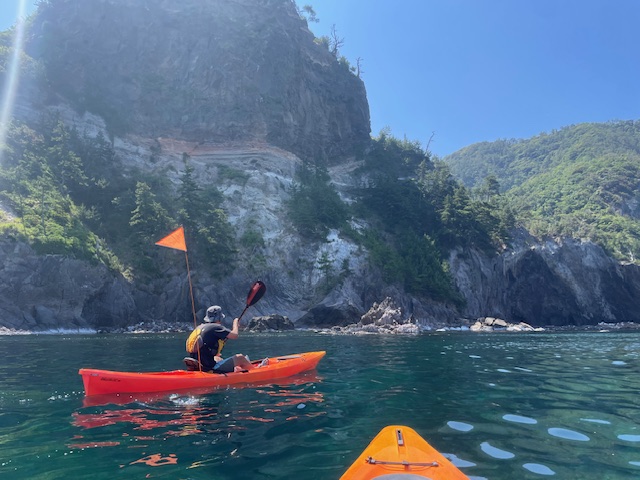 晴天のもと、崖となっている海岸を背景に赤いカヤックを漕いでいる様子の写真