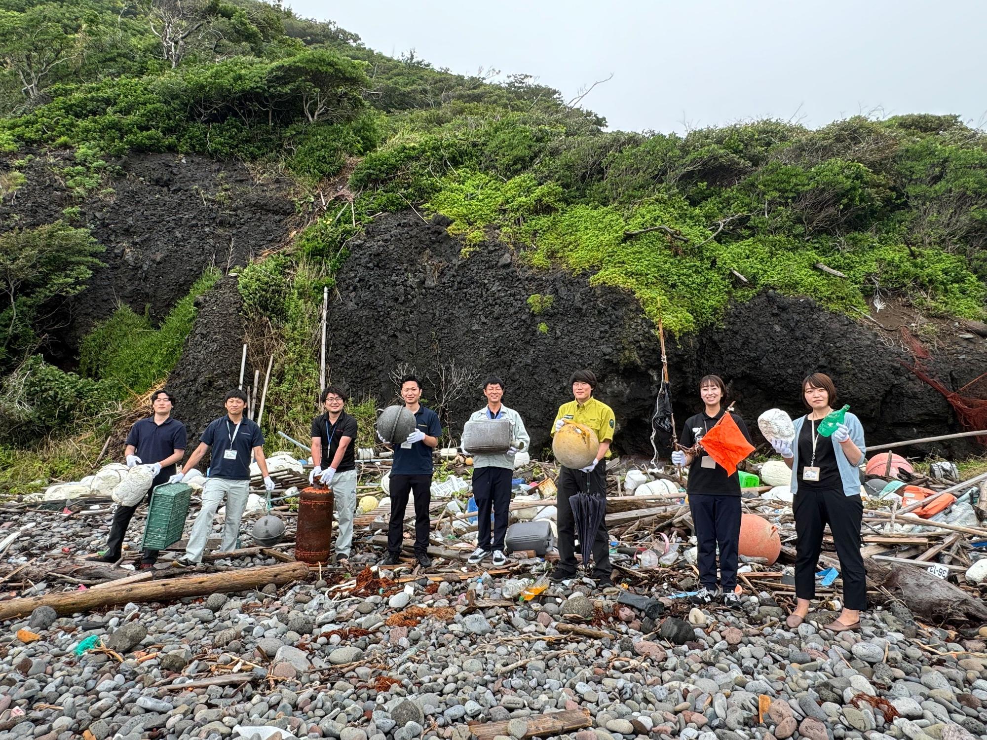 集まったごみの前で回収したごみを持っている8人の参加者の写真