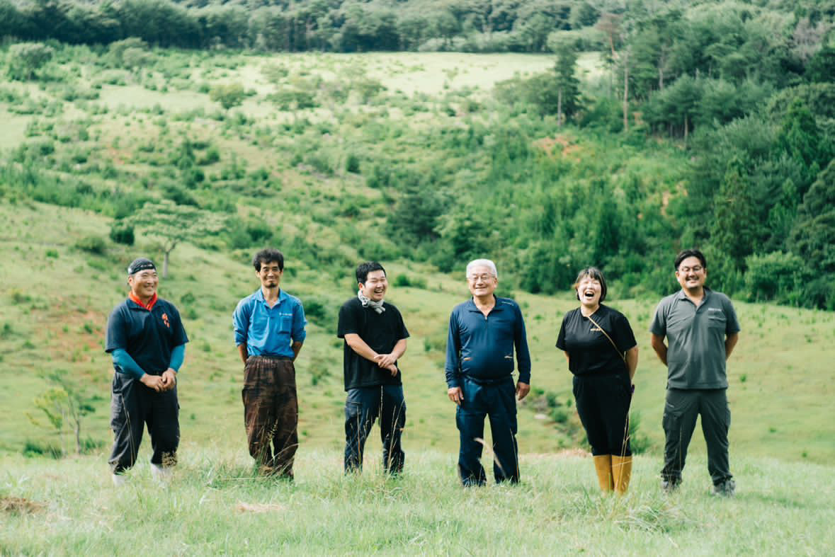 緑の牧草地を背景にした寿畜産の従業員6人の集合写真