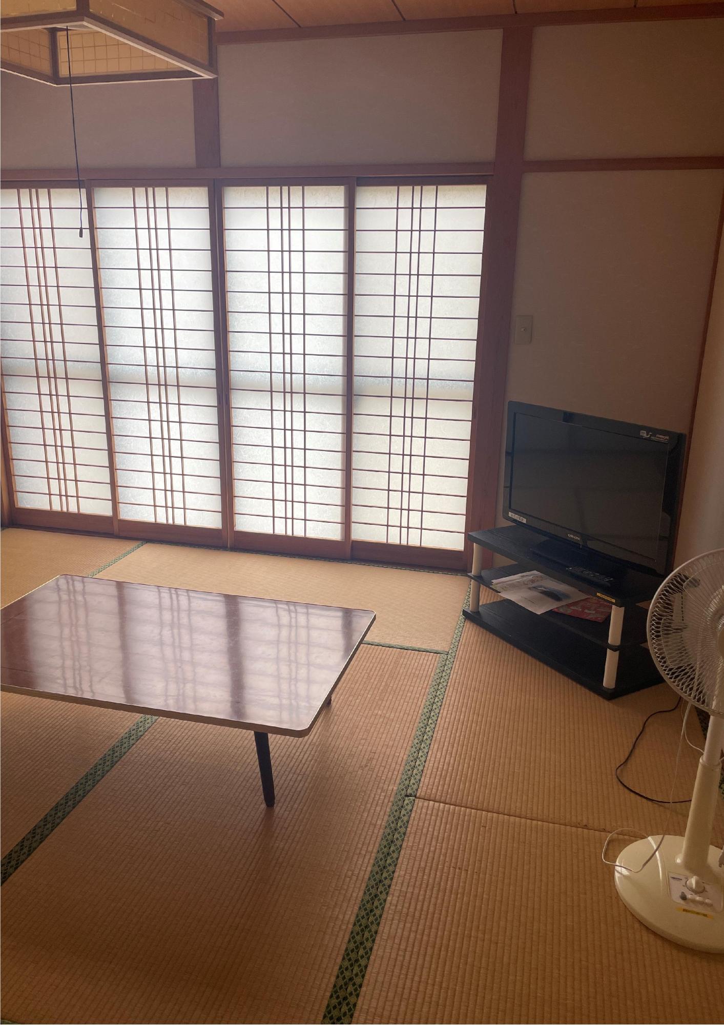 畳が敷かれ、ちゃぶ台とテレビと扇風機がある和室の写真