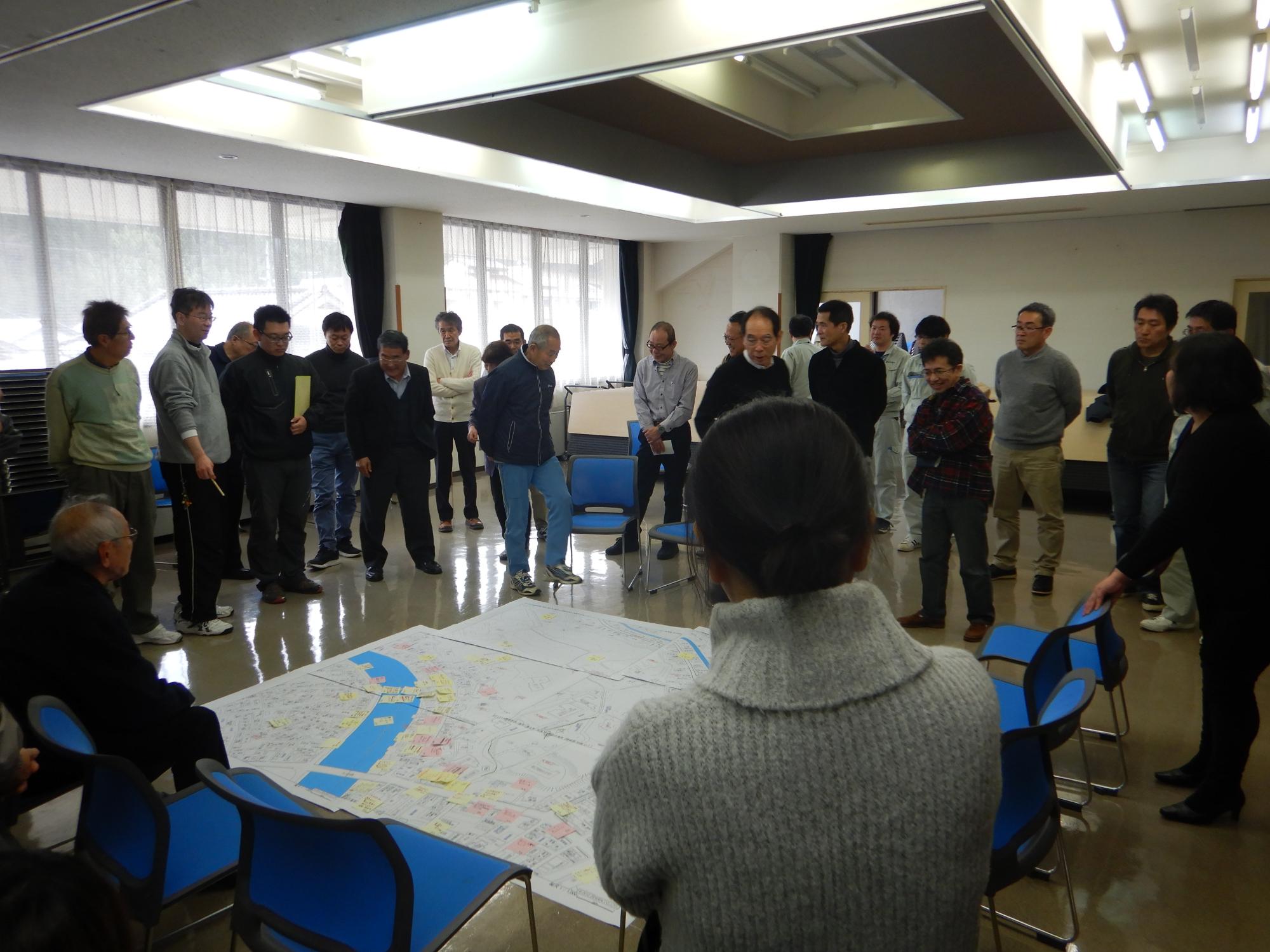 床に置かれた付箋の付いた大きな地図を取り囲む人たちの写真