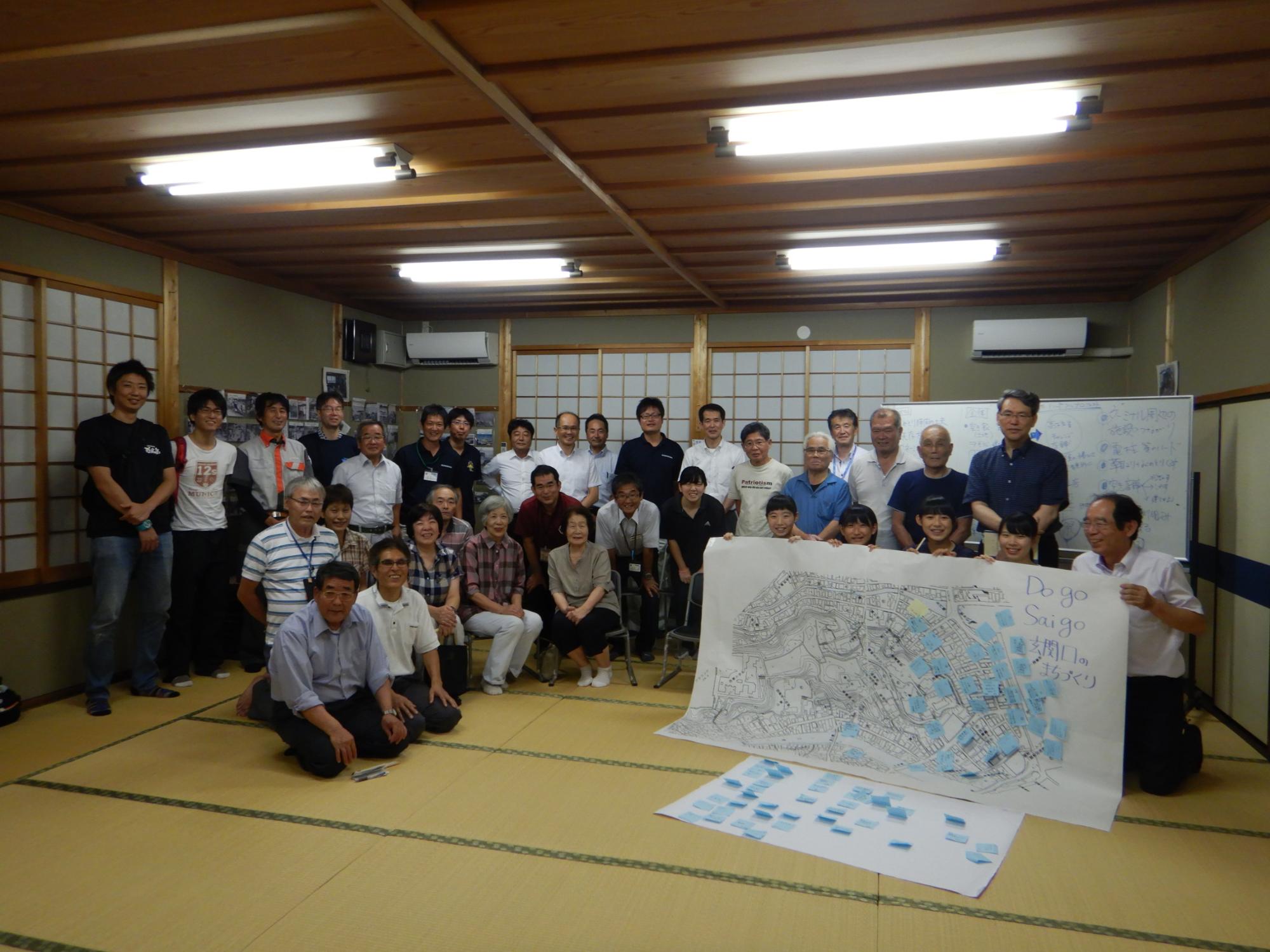 付箋の付いた大きなマップを見せている子供たちと周りに並ぶ大人たちの集合写真