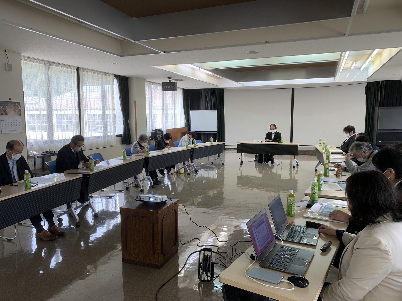 楕円形に並んだ席に座って資料やノートパソコンを見ている人たちの写真