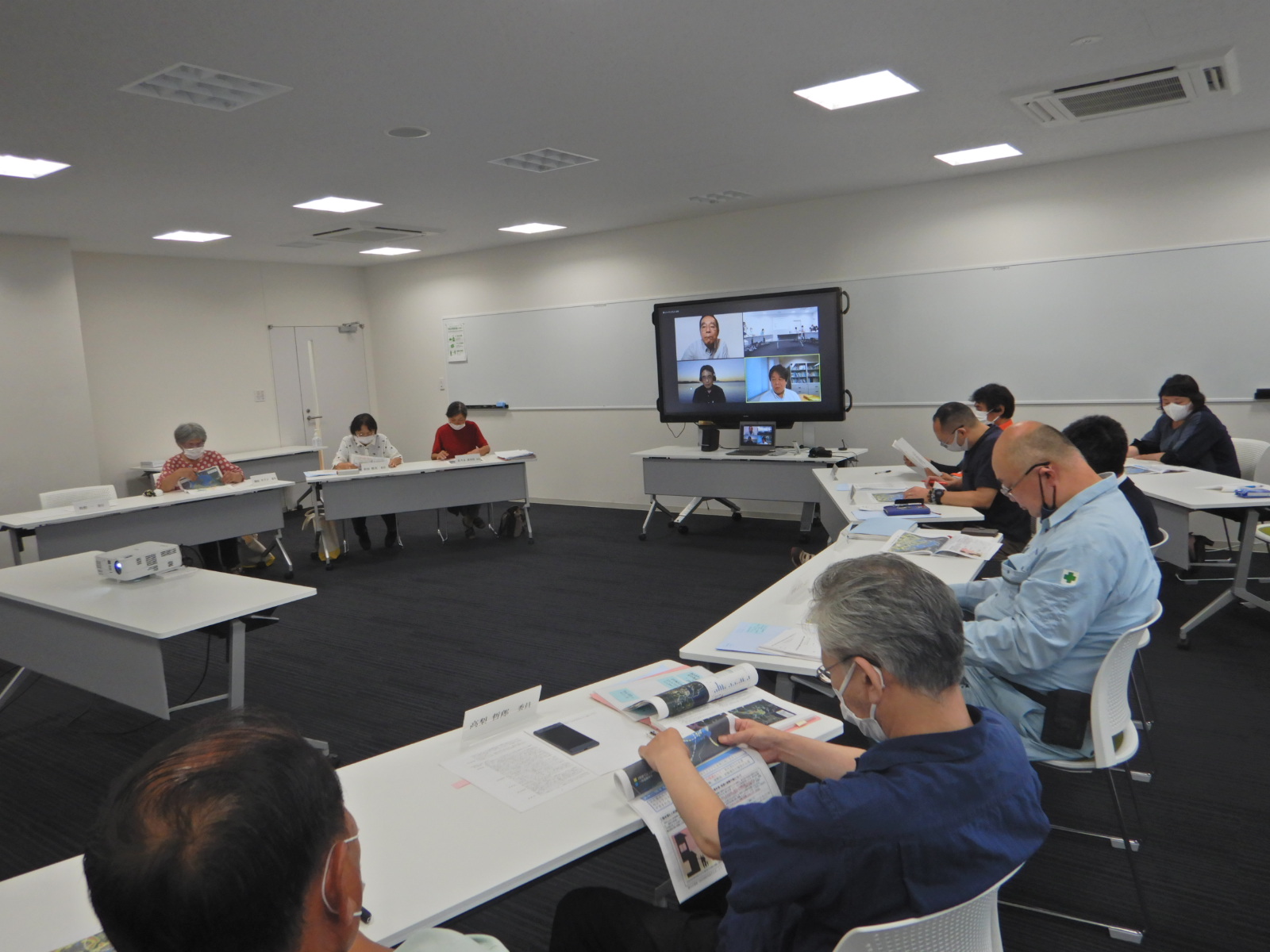 モニターの置かれた会議室で資料を見ている人たちの写真