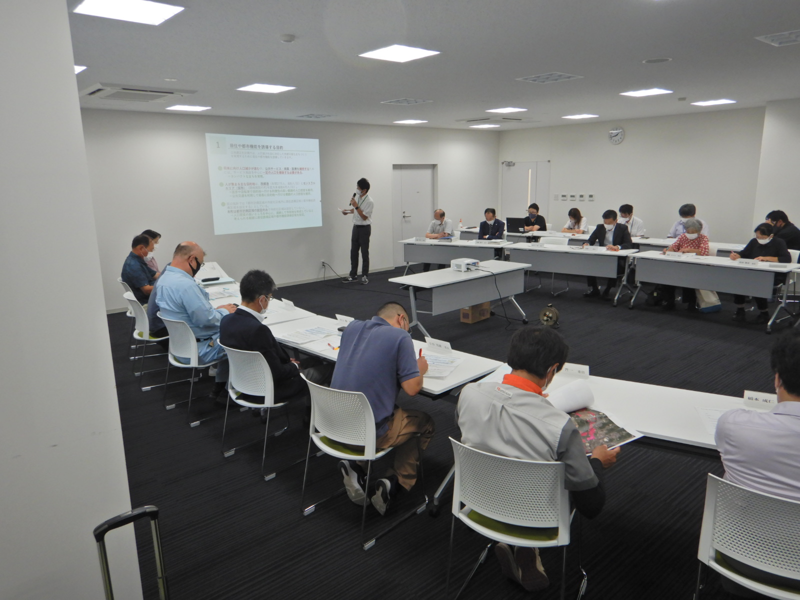 プロジェクターで映した画面を見て話している人と資料に書き込みをしている人たちの写真