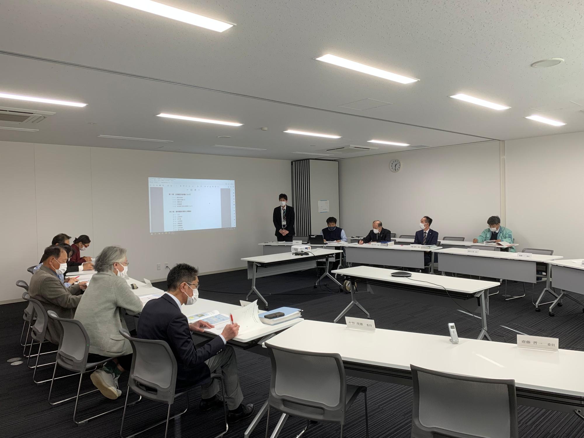 プロジェクターで映した画面を見る人と机の資料を見ている人たちの写真