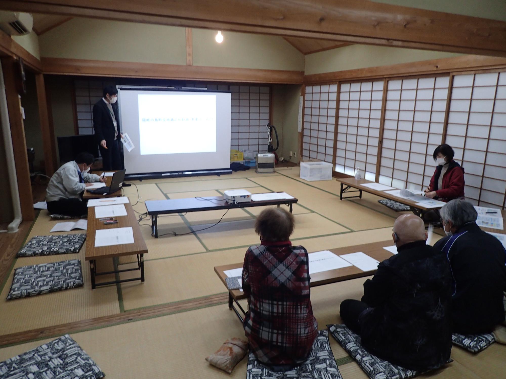 座敷の部屋で座っている複数の人が前方のスクリーンを見ている写真