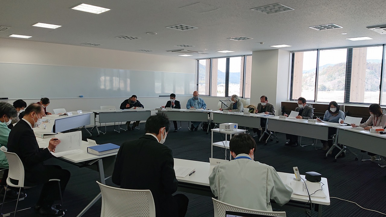 楕円形に並んだ席に座って資料を確認している人たちの写真