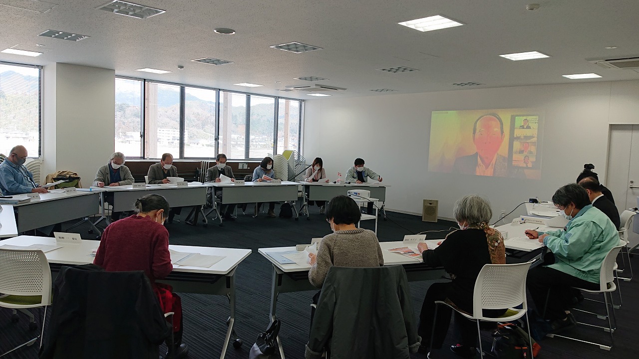 プロジェクターの映像が映った部屋で席に座って資料を見ている人たちの写真