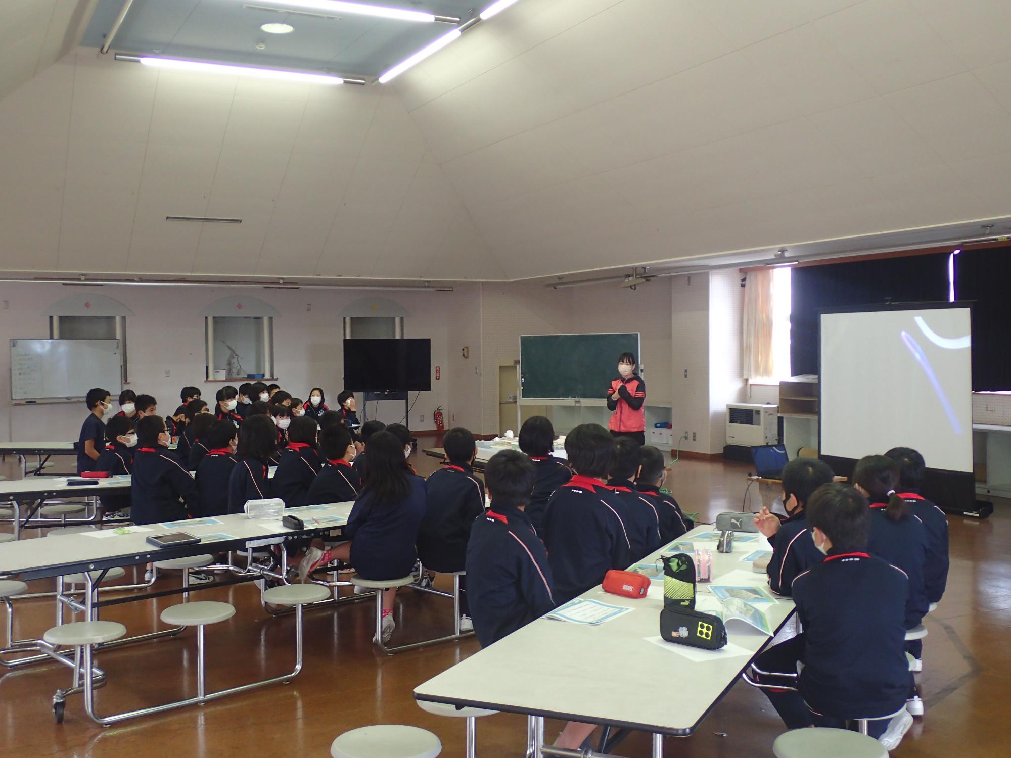 前方に立つ女性の話を聞くジャージ姿の生徒の後ろ姿の写真