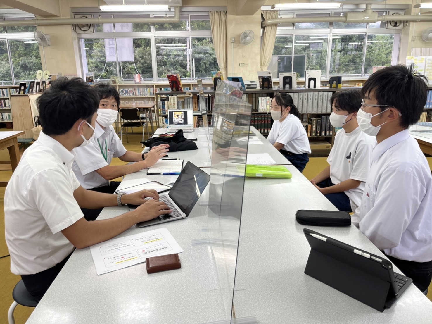 マスク姿で向かい合って座る生徒たちの写真