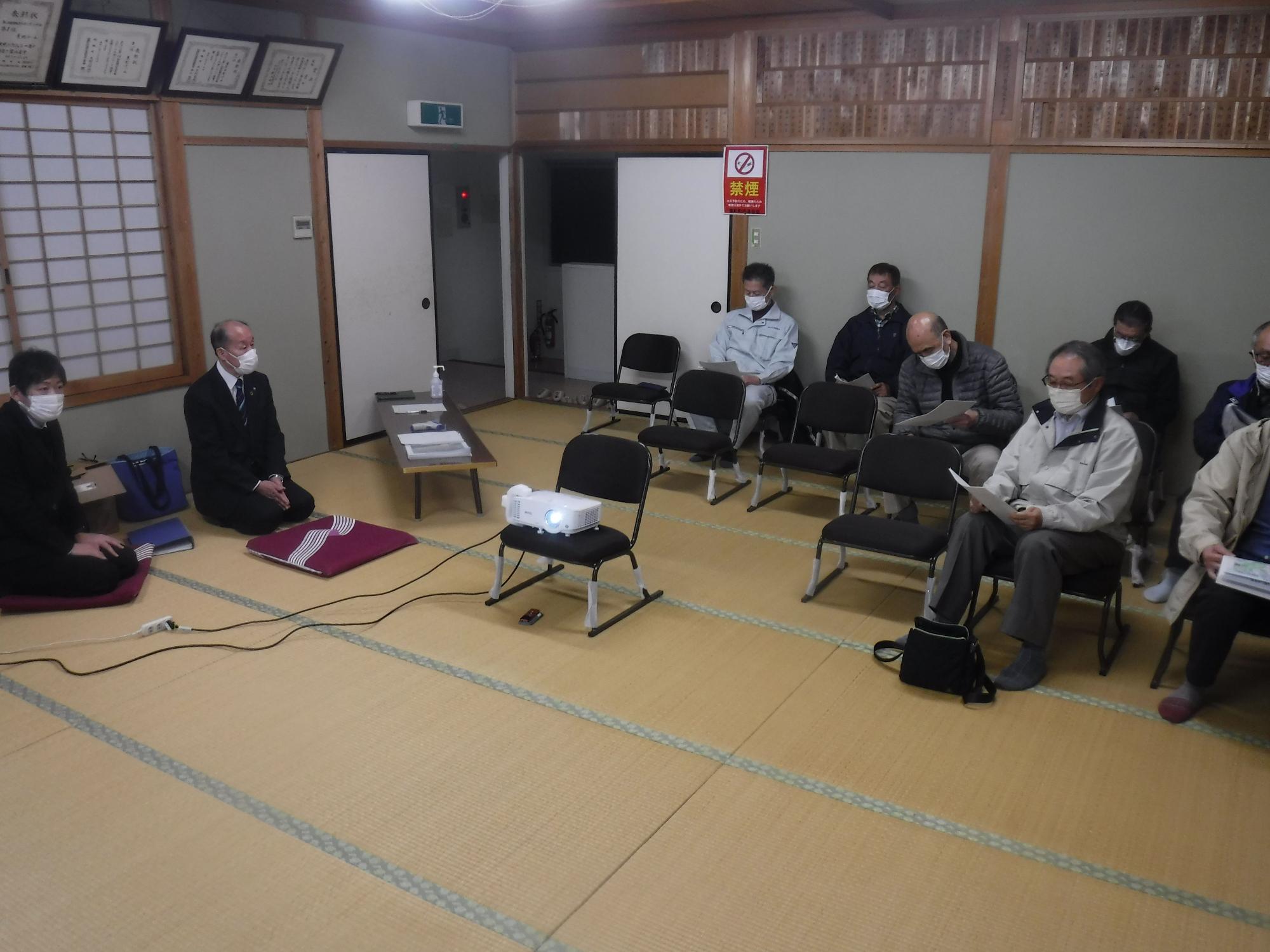 座敷の部屋で複数の人たちが椅子に座って書類を見ている写真