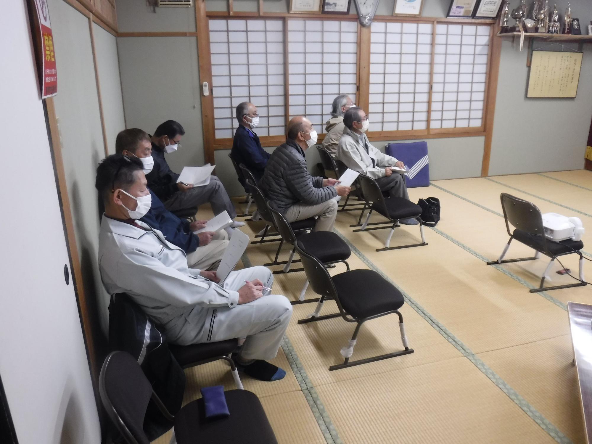 座敷の室内で椅子に座り手元の書類を見る複数の男性の写真