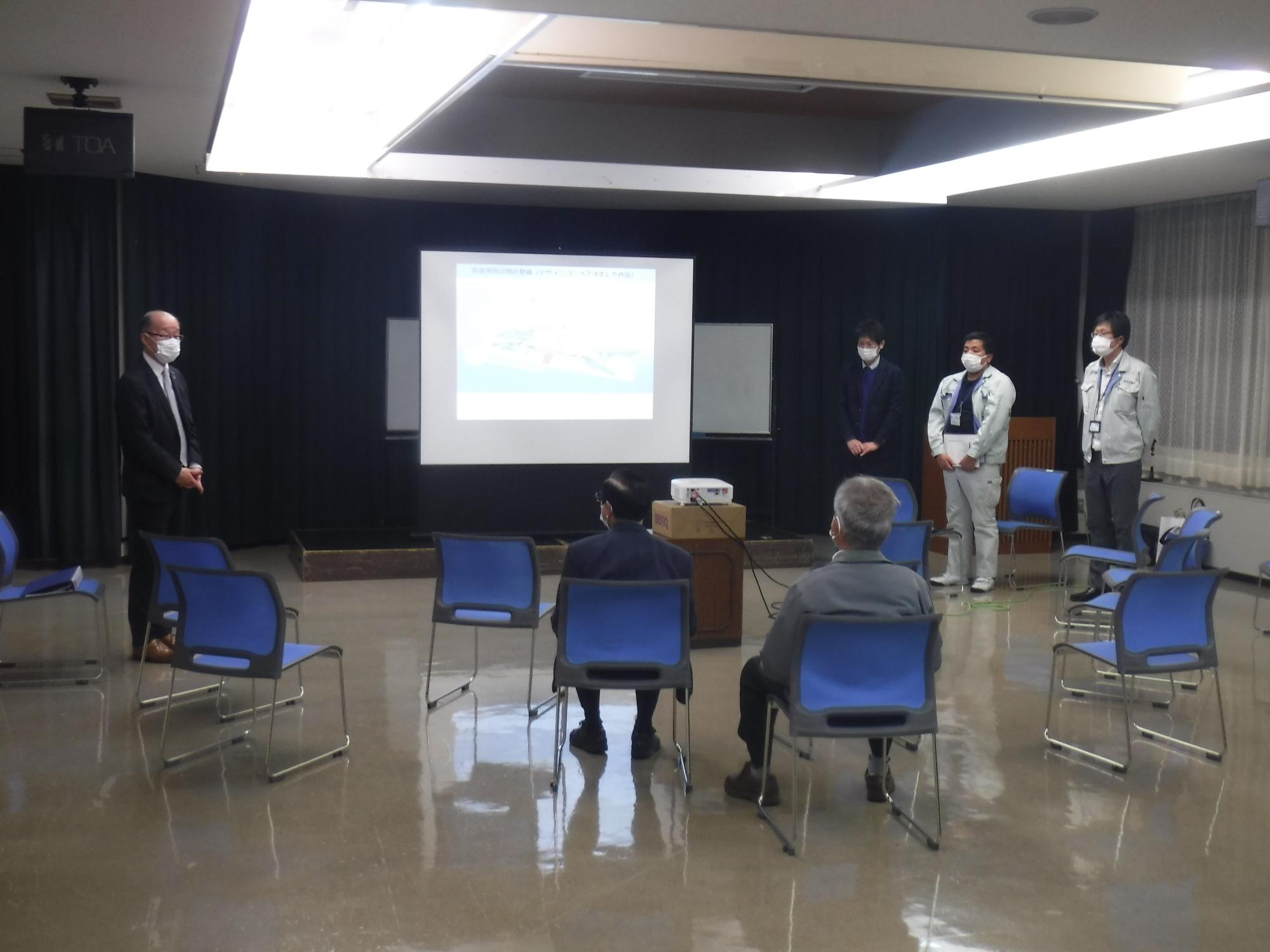 スクリーンの両脇に男性4人が立っている写真