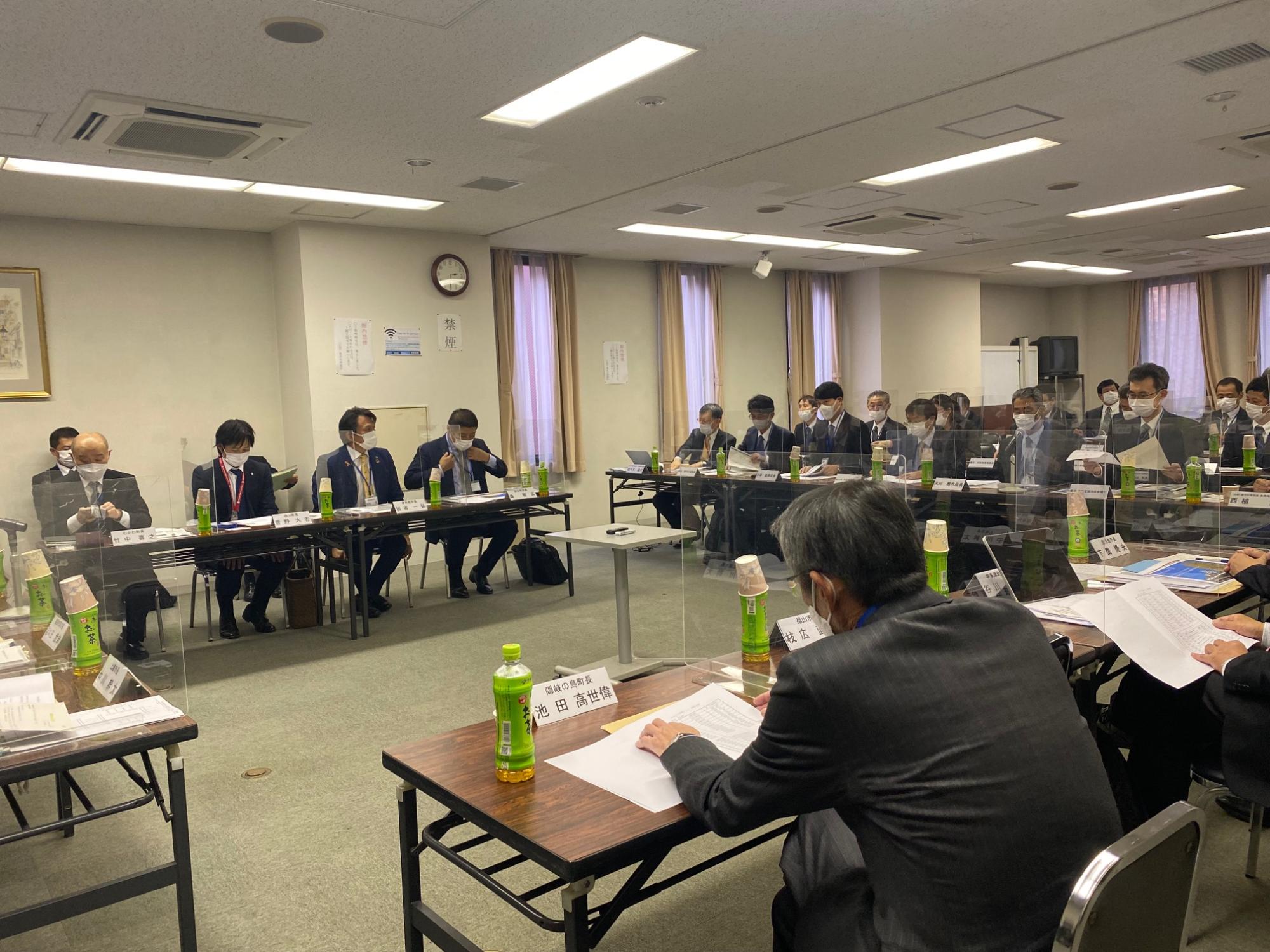 アクリル板で仕切られた席に座って資料を確認するスーツ姿の人たちの写真