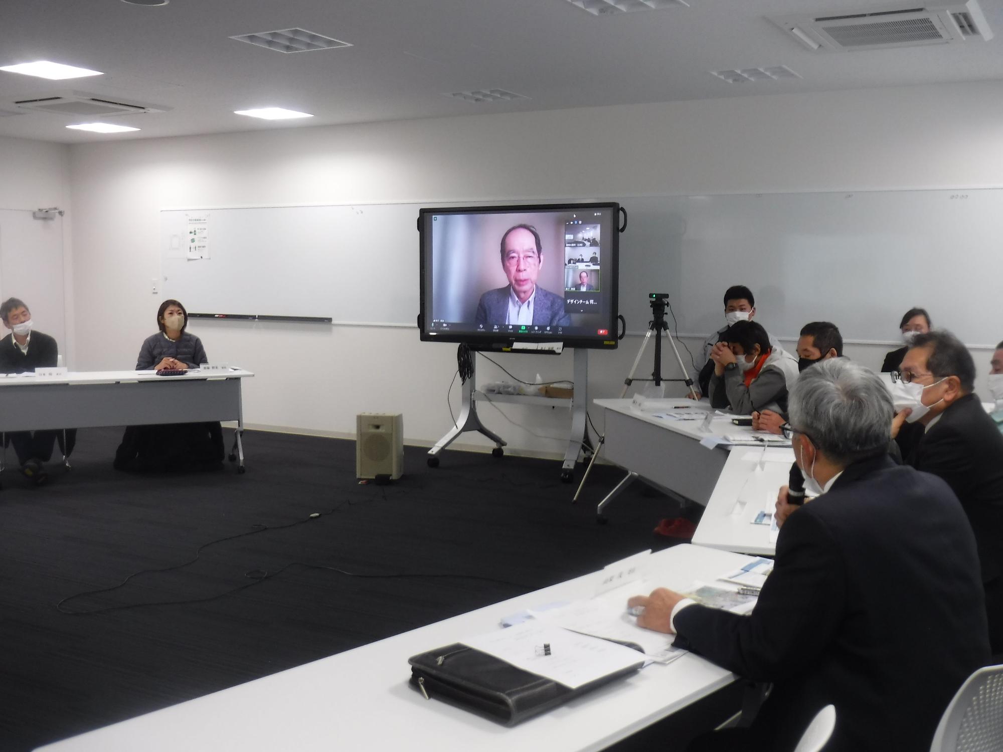 男性がマイクを手に持ちモニターに映る男性と話している写真