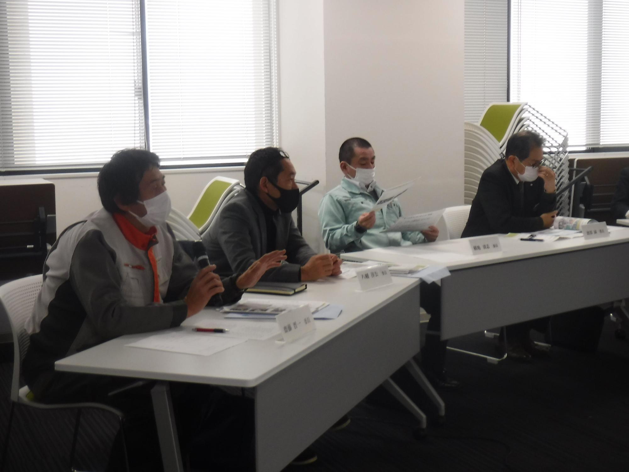 資料の置かれた席に座るマスクを着用した男性4人の写真