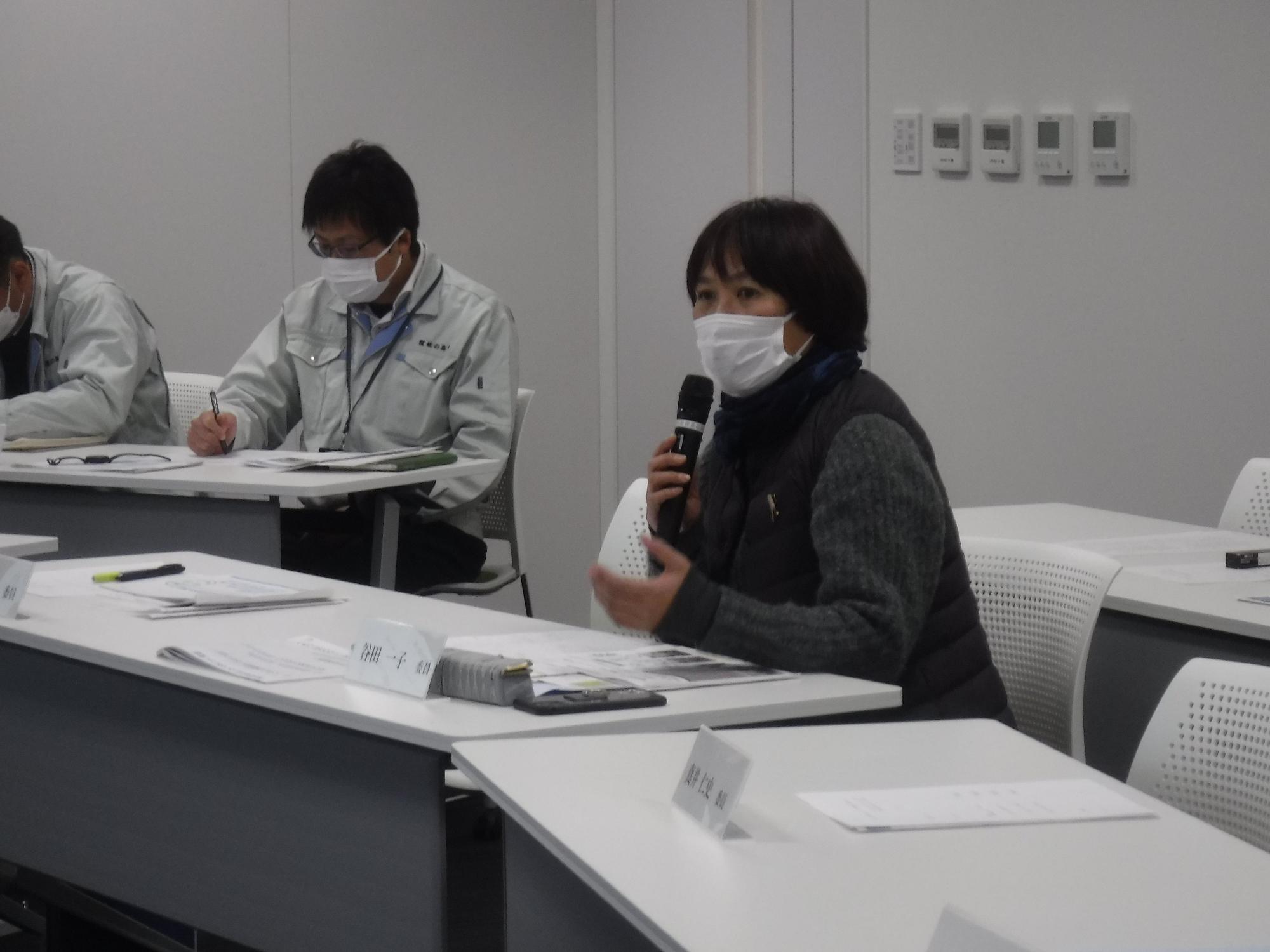 マイクをもって座ったまま話すマスク姿の女性の写真