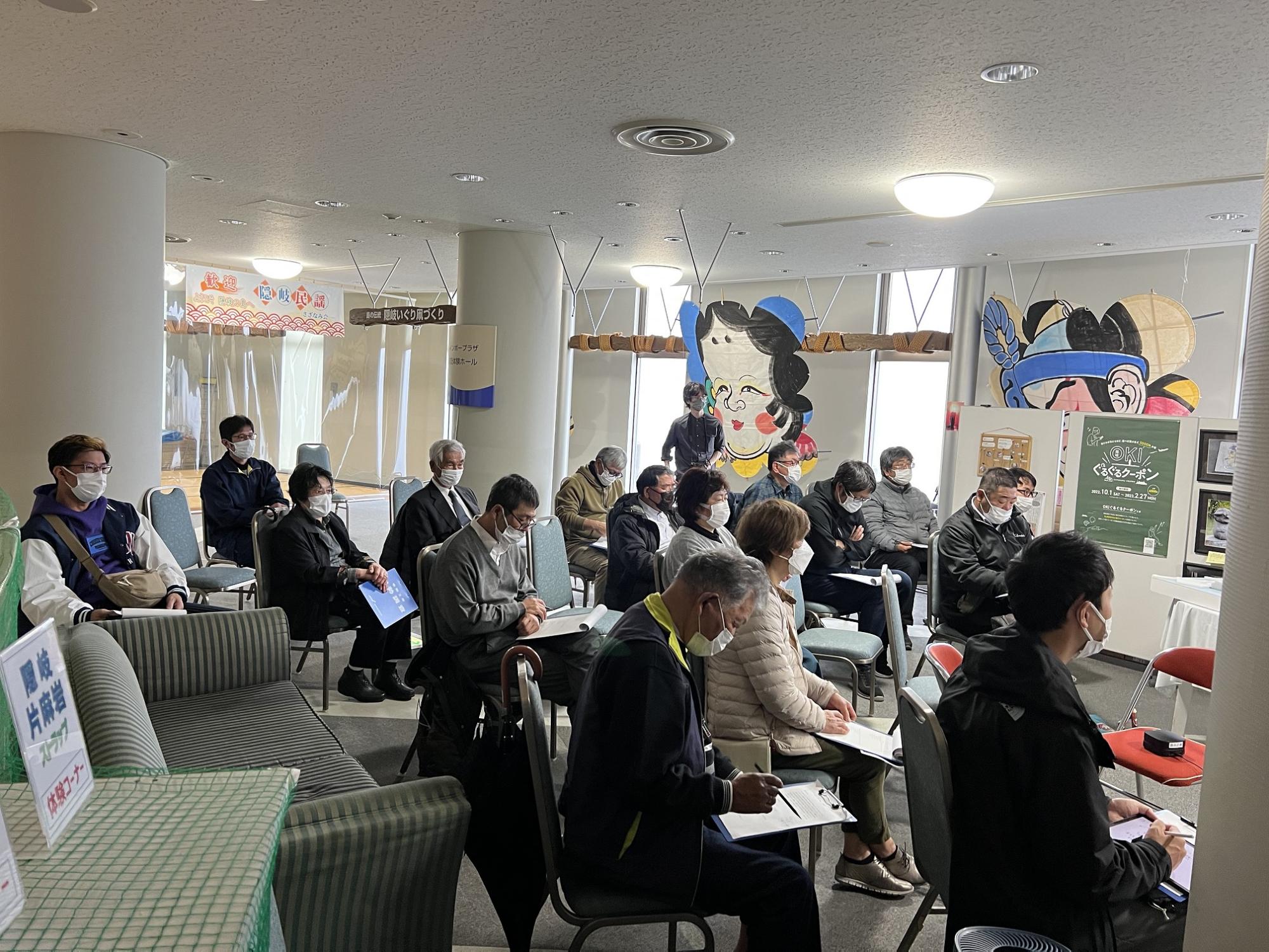 椅子に座った人たちがメモを取りながら話を聞いている写真