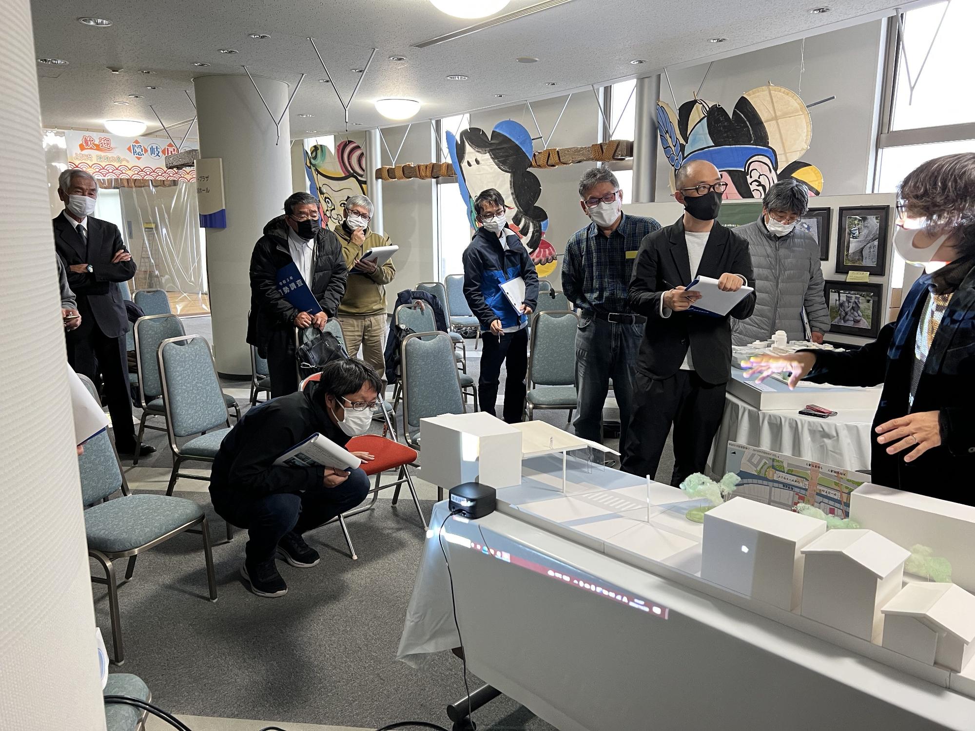 建築模型の横でバインダーをもって話をしている人たちの写真