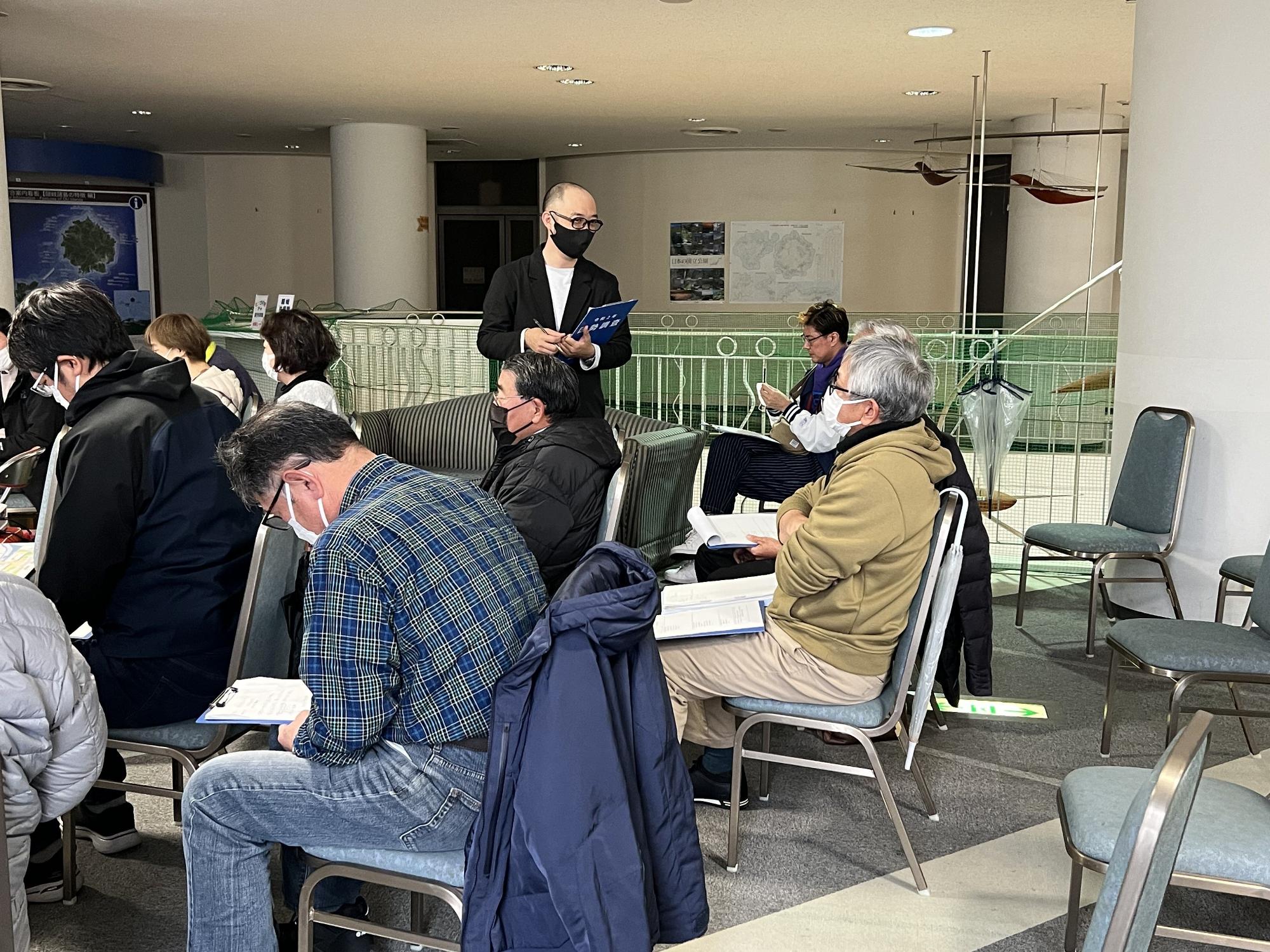 椅子に座った白髪の男性と立った黒マスクの男性が話をしている写真